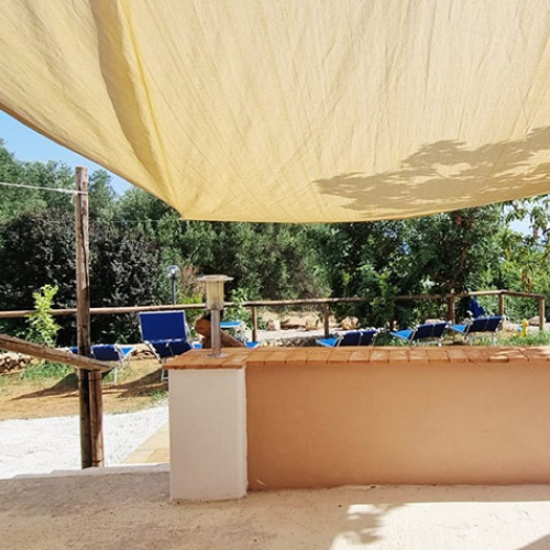Terrazza soleggiata con tende e sedie blu, immersa nel verde rigoglioso.